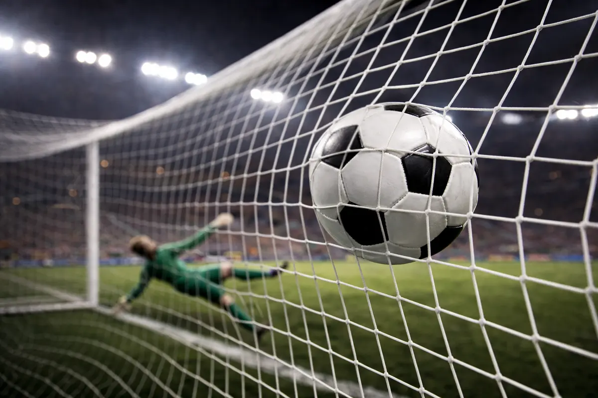 Pallone da calcio che entra nella rete di una porta durante una partita serale di Europa League con i riflettori dello stadio accesi